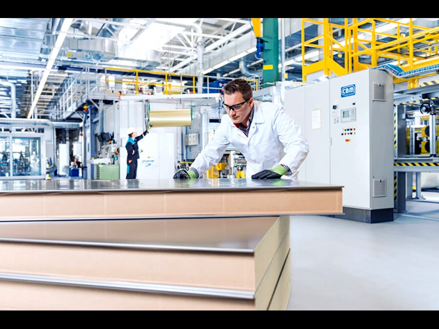 Factory employee in a lab coat inspecting several panels inside a factory hall.