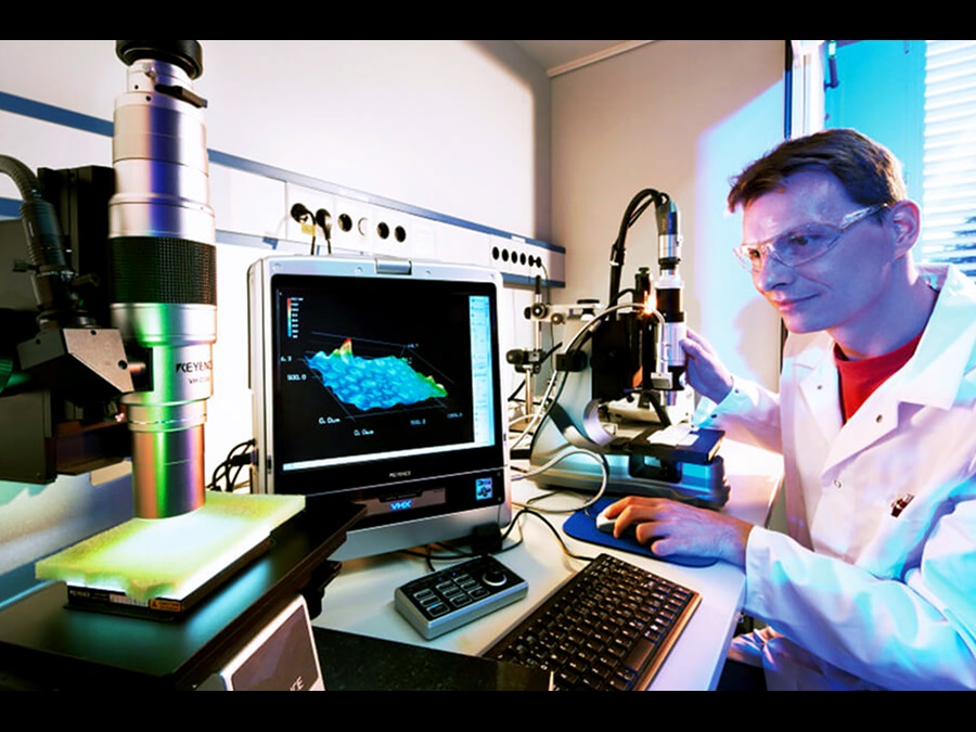 An employee in a lab coat working in the field of research and development with a computer and a microscope.