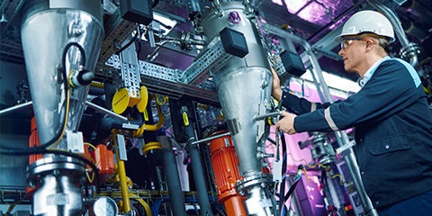 A factory employee wearing protective working clothes is operating a machine.