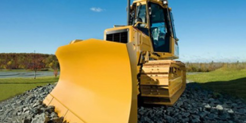 Yellow excavator on an earthy field with trees in the background.