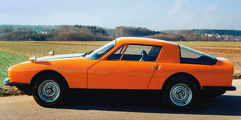 Side view of an orange sports car in front of a field.