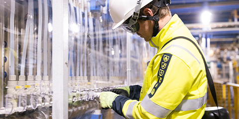 An employee in protective clothing and helmet inspects various hoses in a factory hall.
