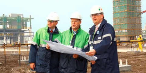 Three construction workers wearing hard hats inspect construction plans on a building site.