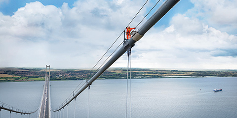 Frontal view of a bridge from above with a worker on the bridge cables.