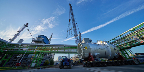 Factory with cranes in front of a bright blue sky.