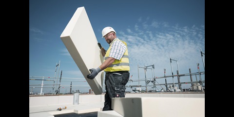 Arbeiter in Schutzkleidung trägt eine Dämmplatte.